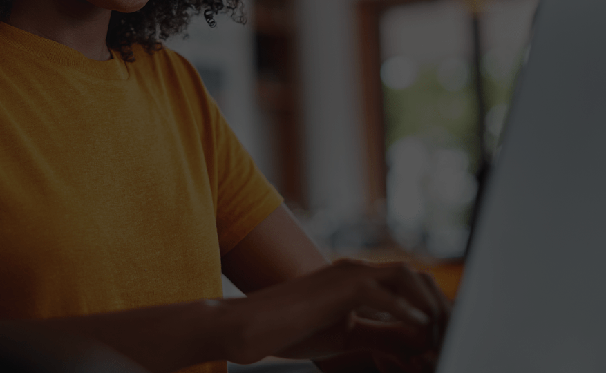woman in orange shirt typing at a laptop