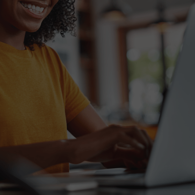 woman in orange shirt typing at a laptop